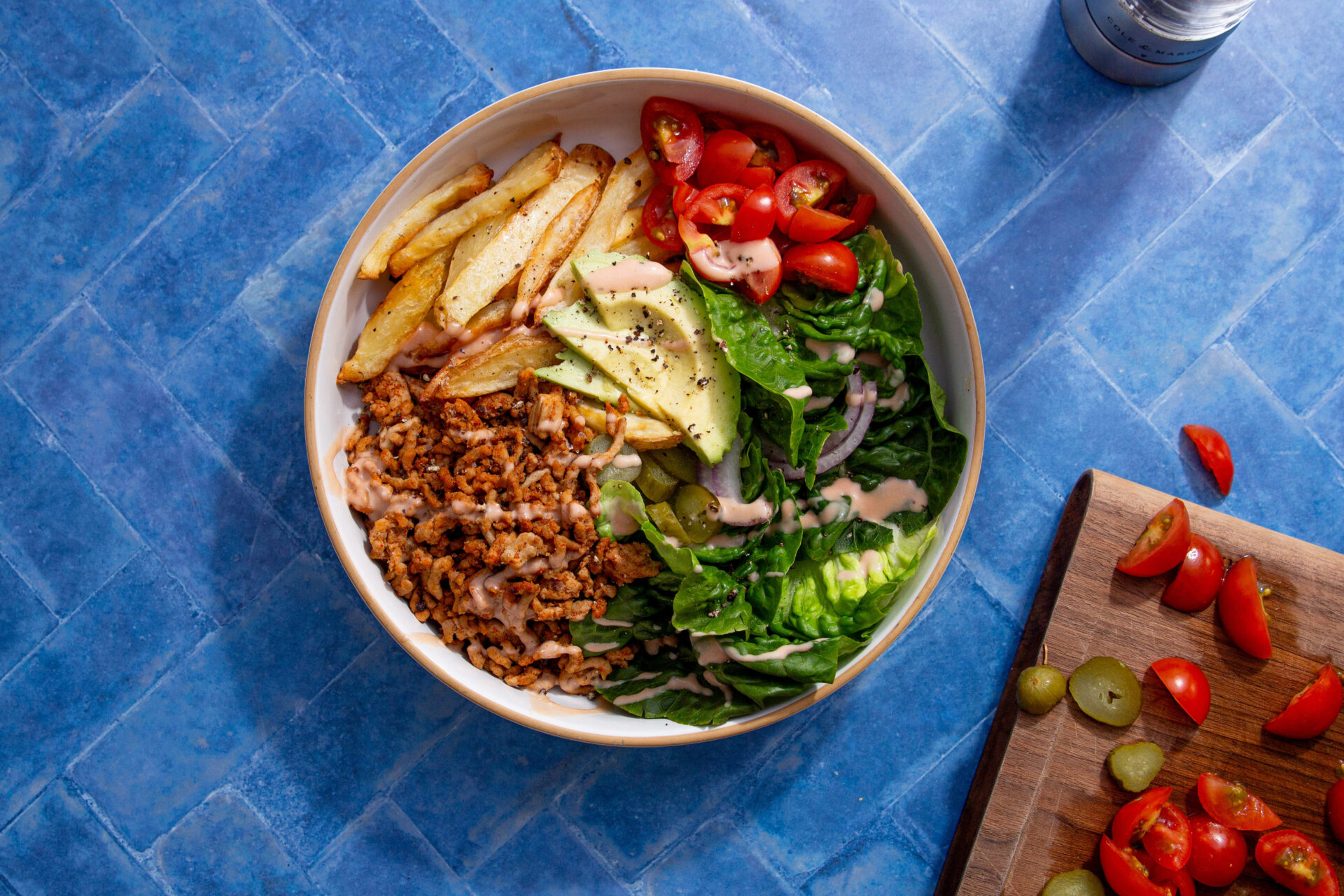 A deconstructed burger-style bowl with chips, pork mince, lettuce, avocado, and tomatoes.