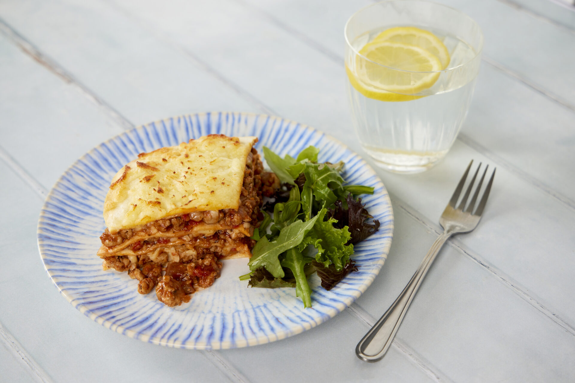 A dish holding a stack of tortillas, stuffed with pork mince, with greens on the side.