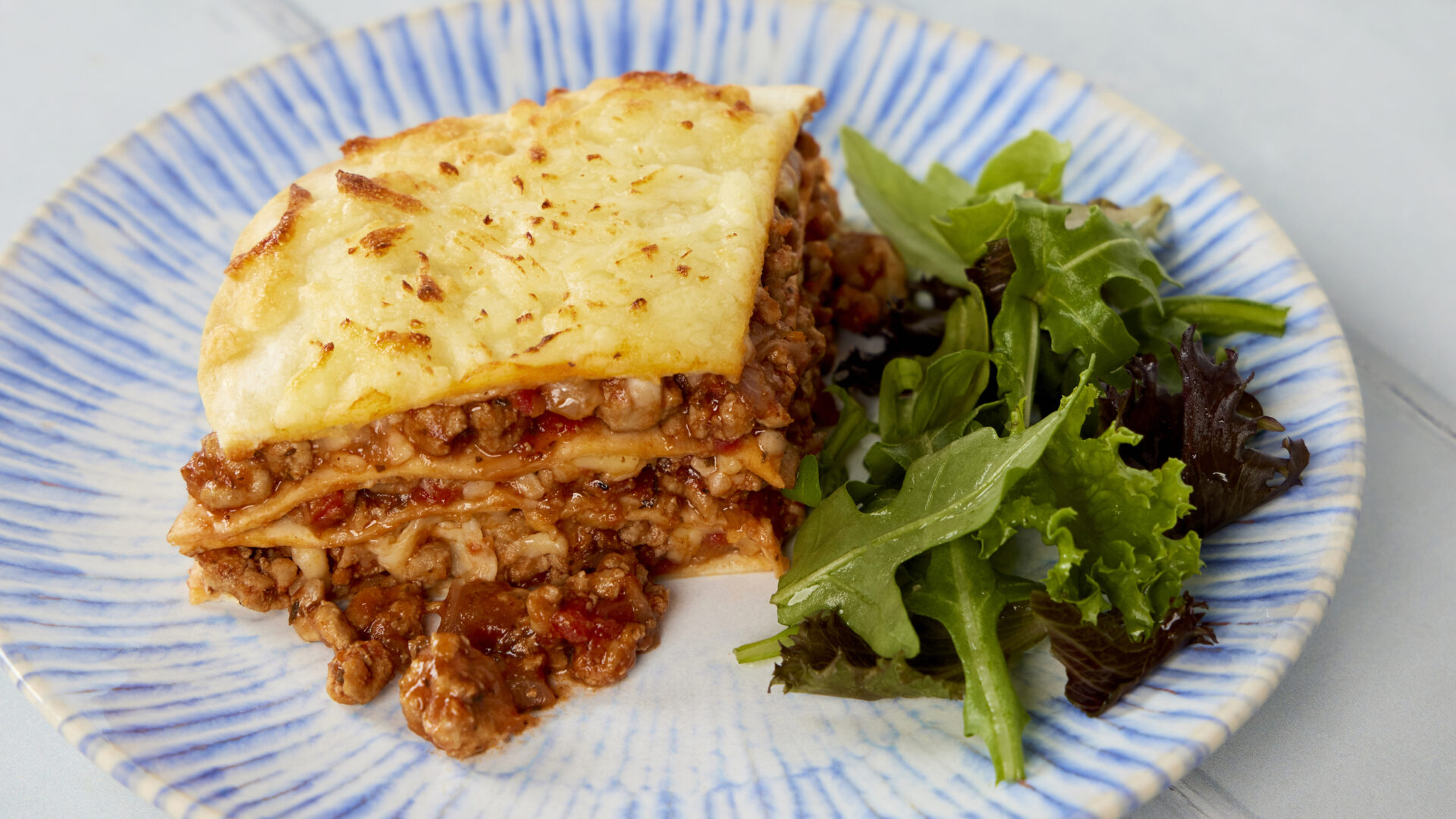 A dish holding a stack of tortillas, stuffed with pork mince, with greens on the side.