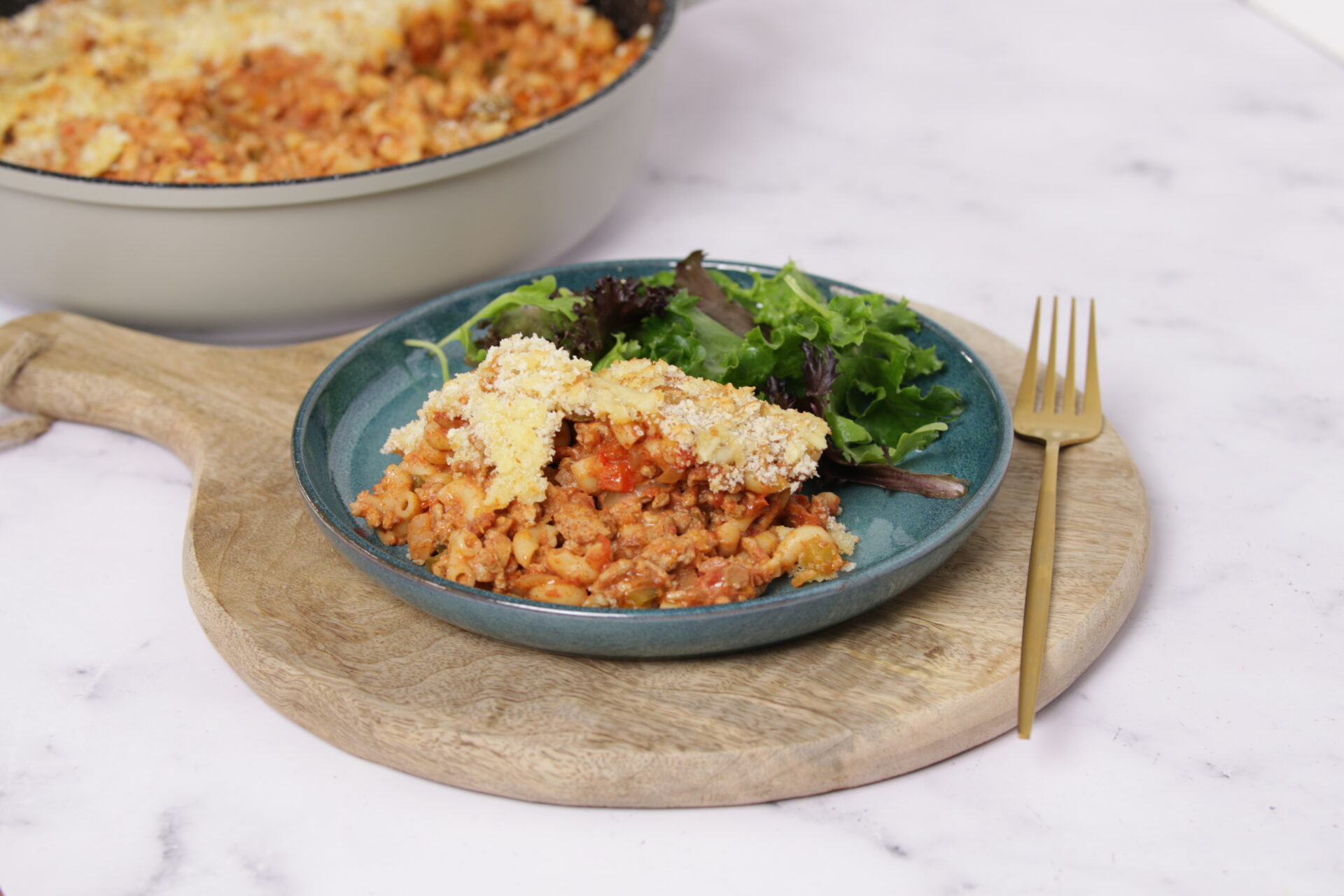 A dish containing pork mac and cheese, with greens on the side.