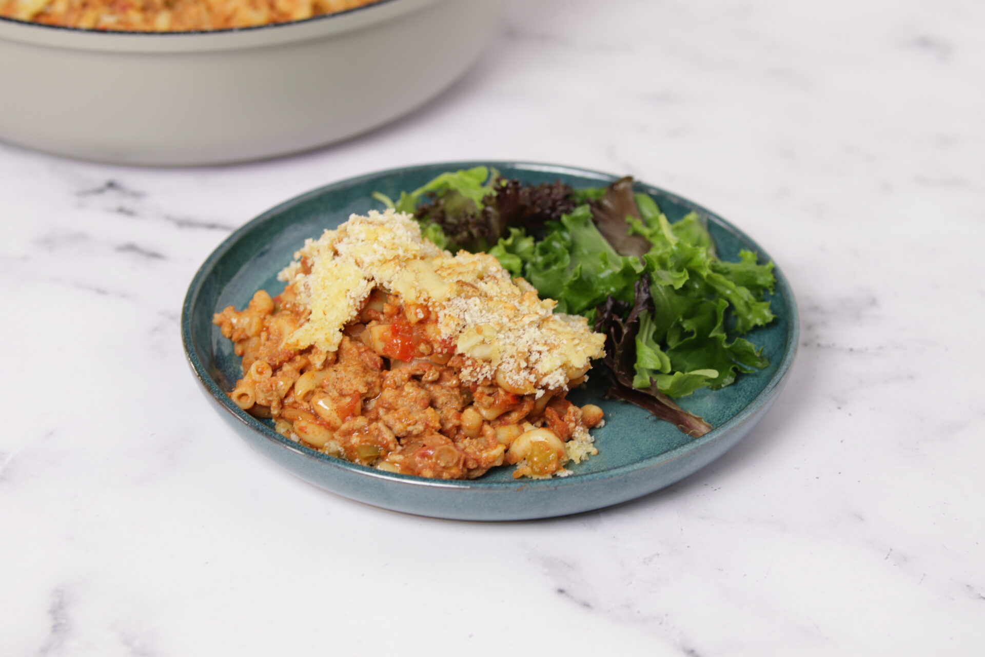 A dish containing pork mac and cheese, with greens on the side.