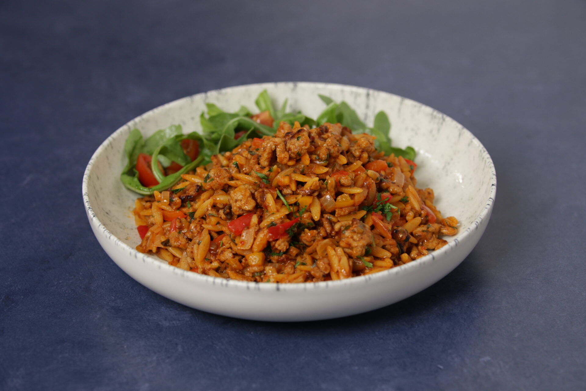 A dish containing pork and chipotle orzotto, with greens on the side.