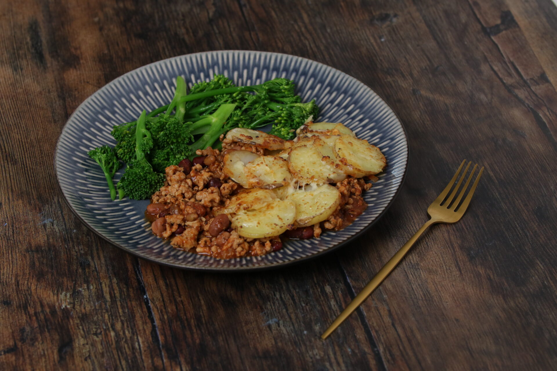 A dish containing cheesy pork hotpot with broccoli on the side.