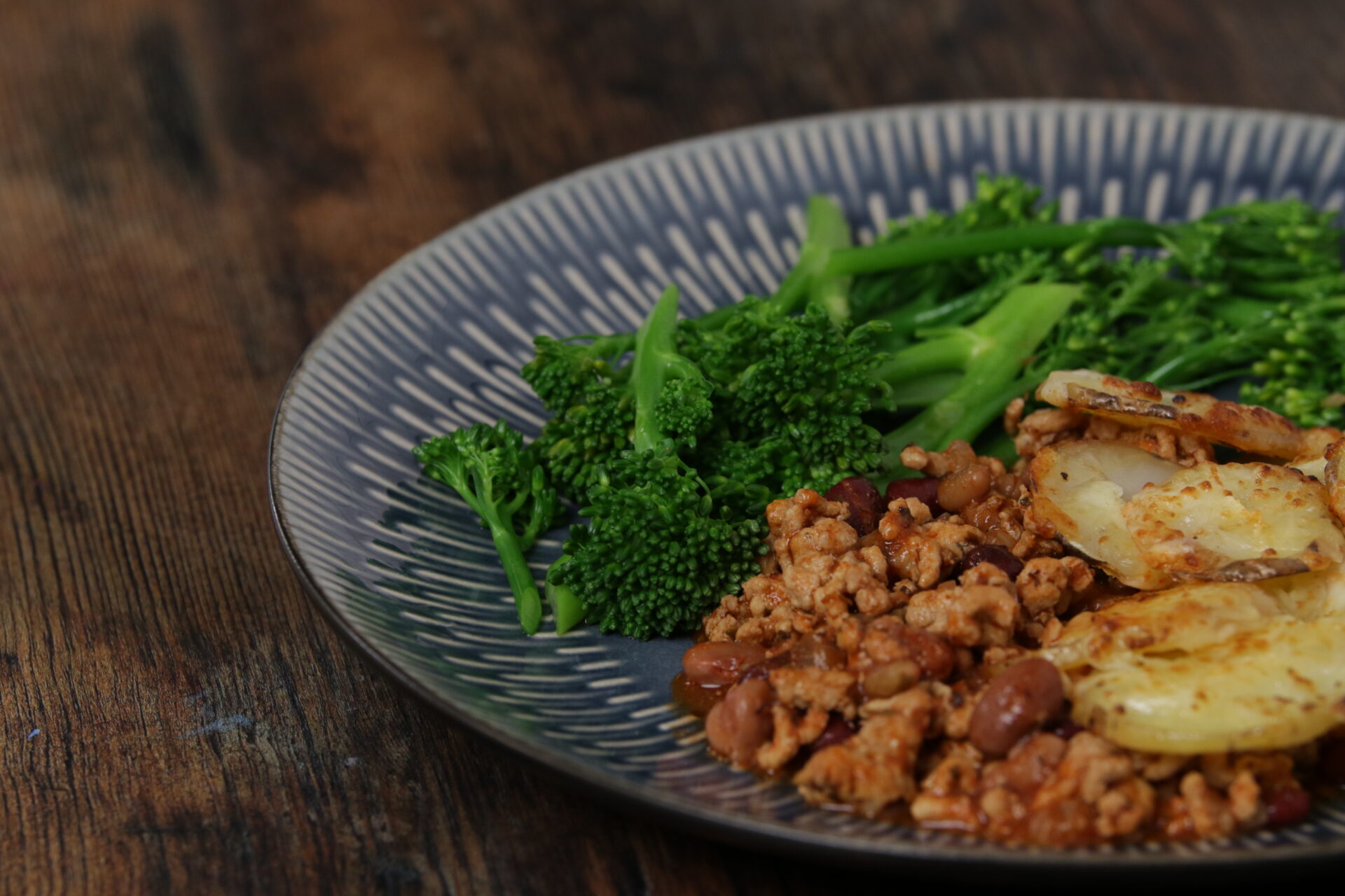A dish containing cheesy pork hotpot with broccoli on the side.