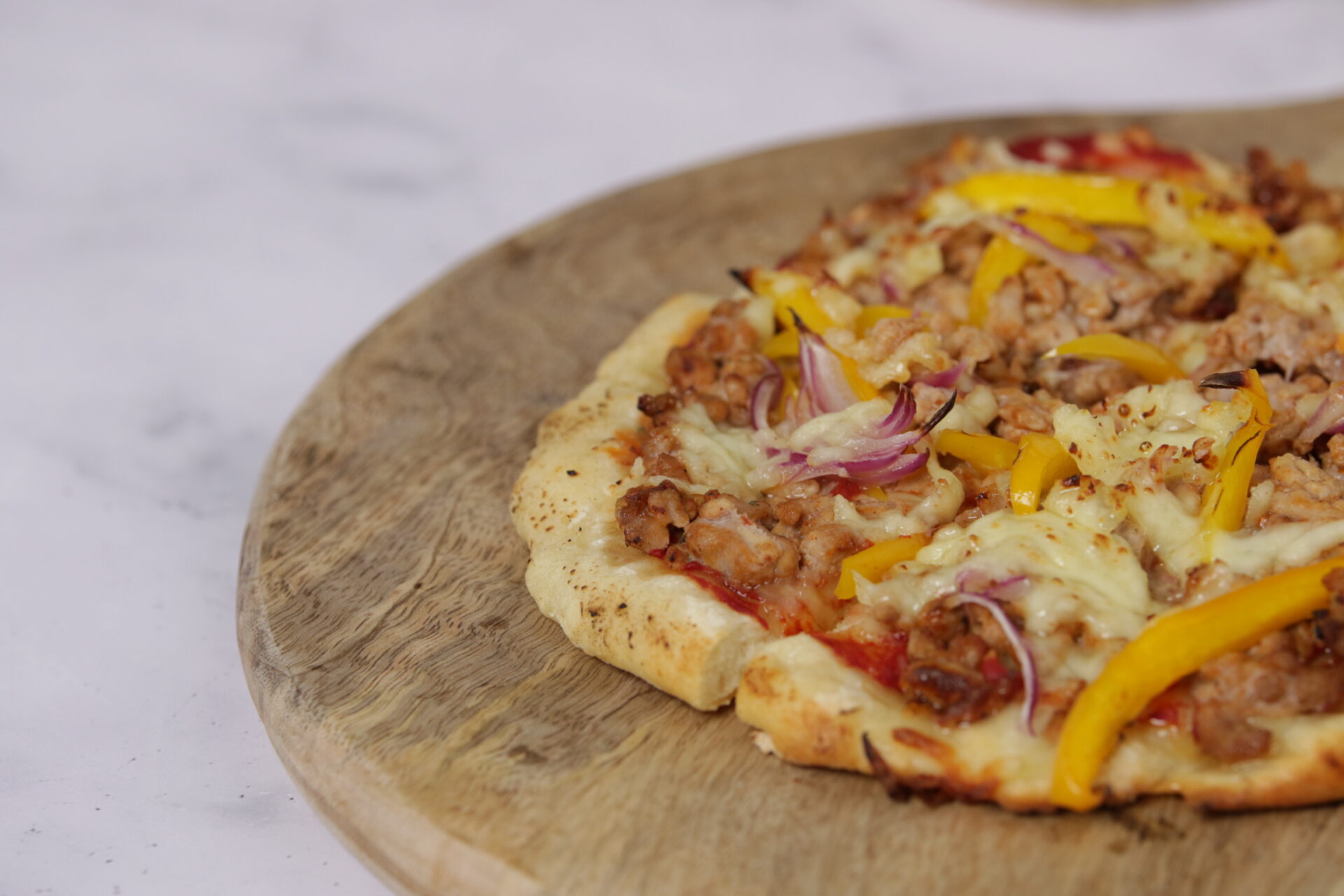 A wooden board that holds a pizza, which is topped with pork mince.