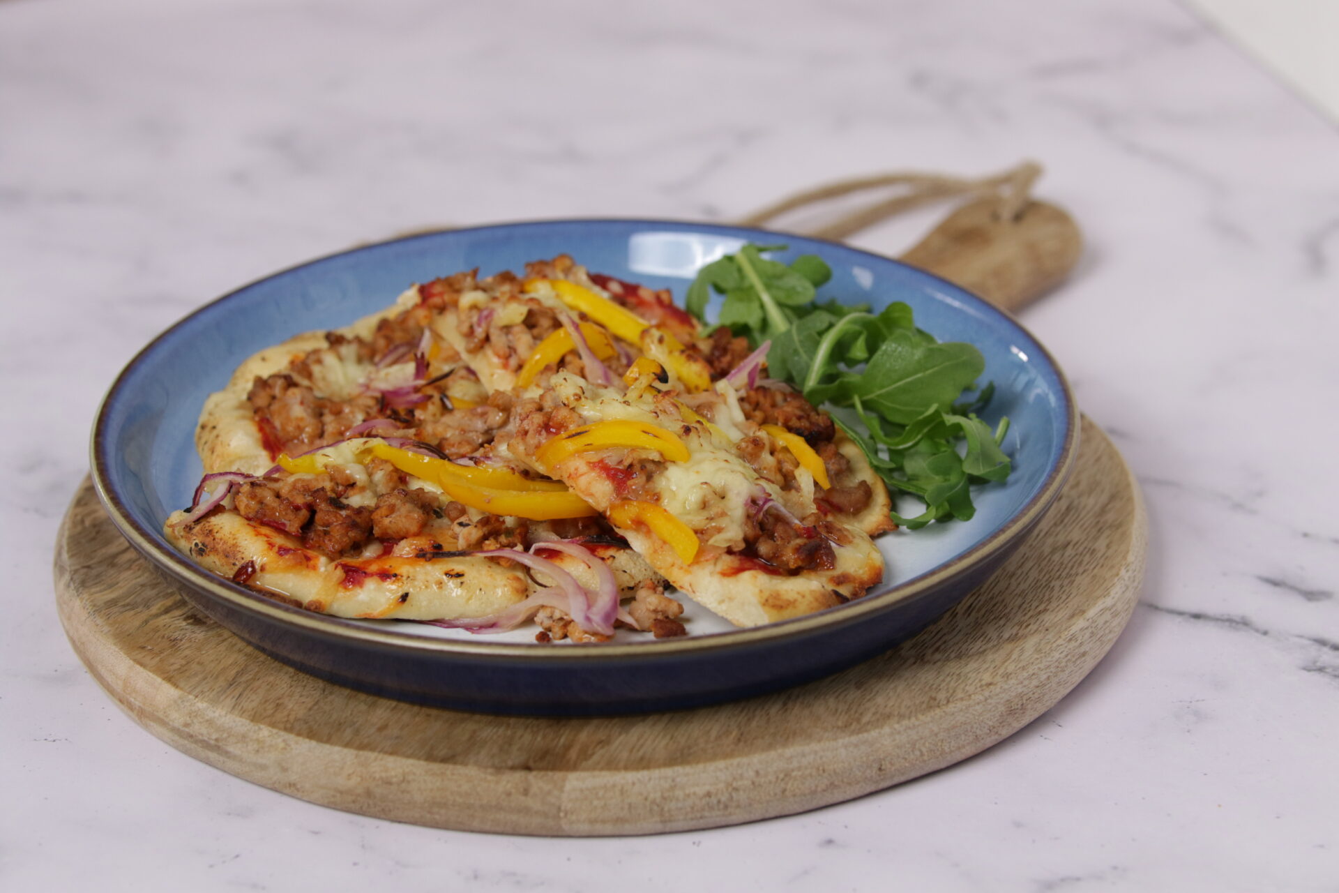 A dish containing pizza, which is topped with pork mince, and greens on the side.