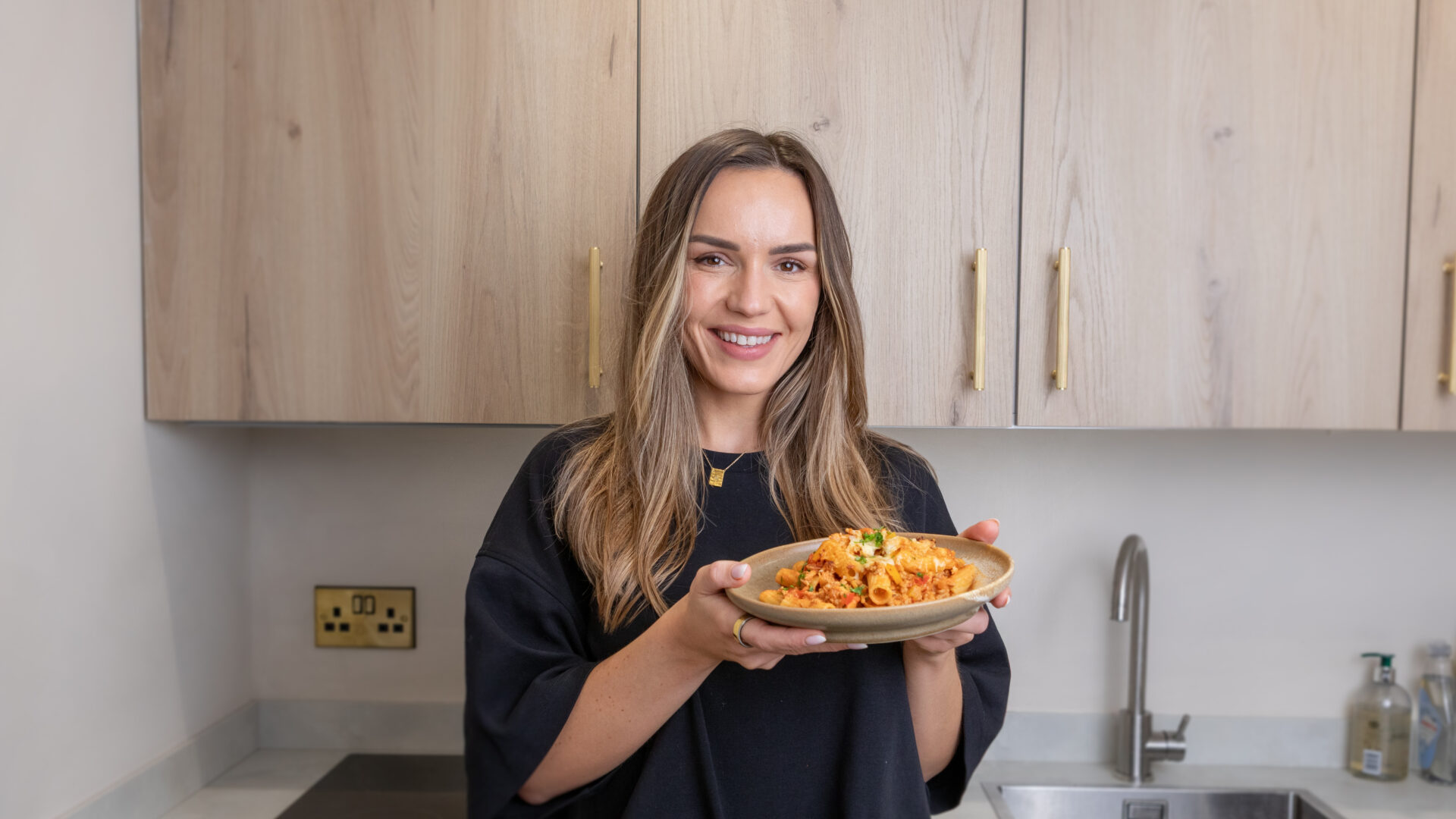 Sarah Hancox holding a plate of Cajun Creamy Pasta Bake in her kitchen.